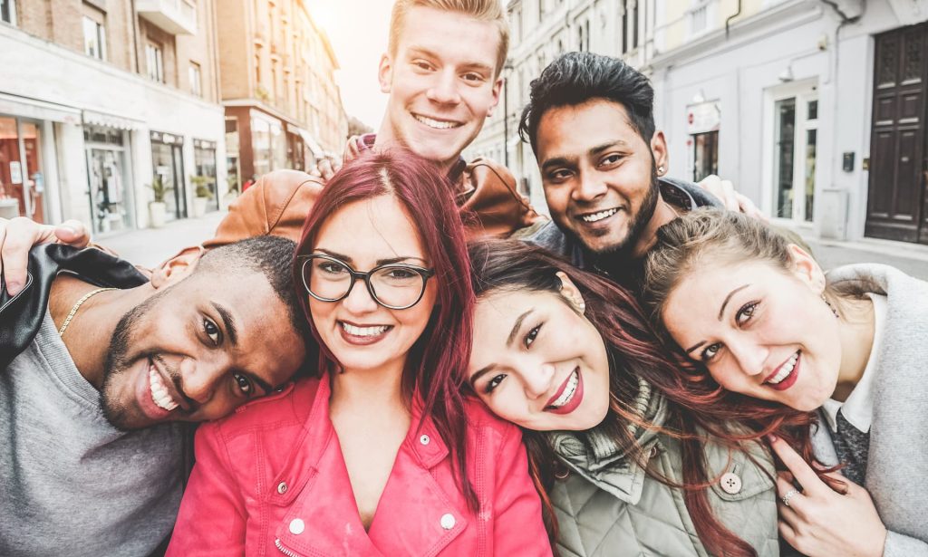 Happy friends from diverse cultures and races taking selfie with back lighting