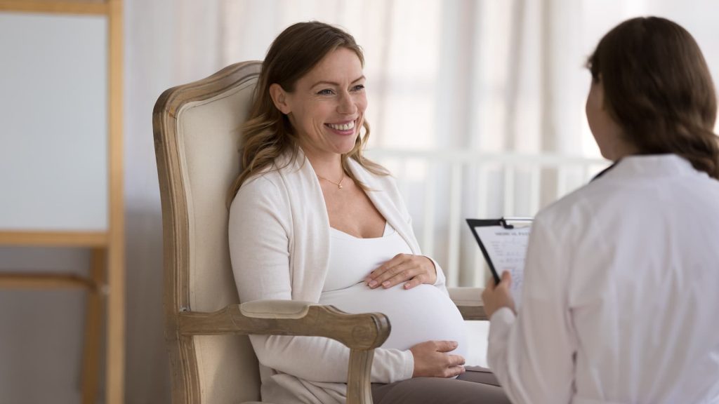 Young smiling pregnant woman patient answers questions of gynecologist during visit at home